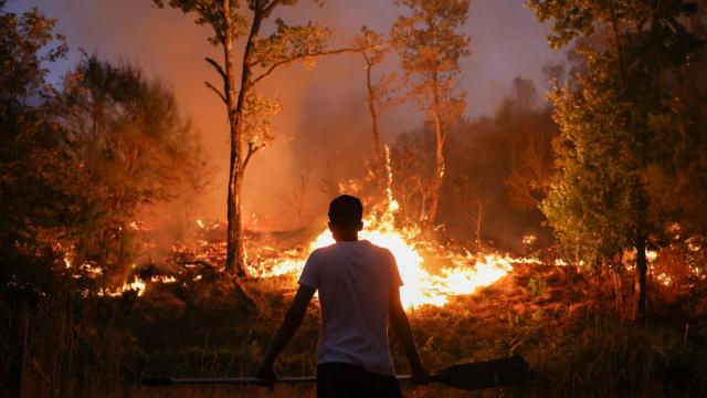 Una persona sostiene una pala mientras las llamas de un incendio forestal aumentan en Vilar de Condes (Orense)