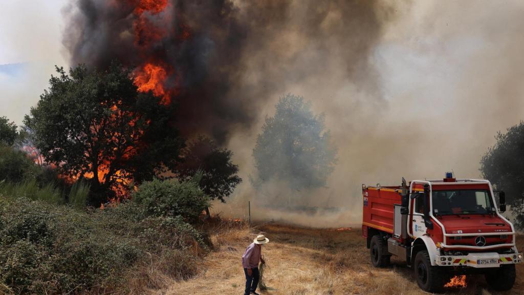Una persona se encuentra cerca de un vehículo de emergencia mientras un incendio forestal arrasa en Veiga das Meas (Orense).