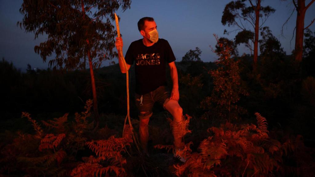 Un vecino con mascarilla sostiene una rama de árbol mientras se produce un incendio forestal en Vilar de Condes (Orense)