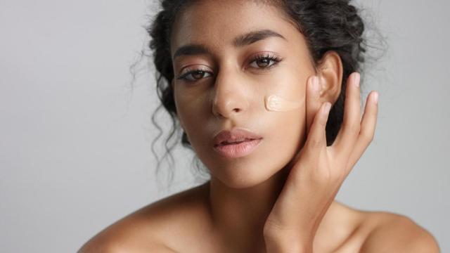 Mujer joven aplicándose base en el rostro.