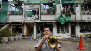 Un estudiante de una escuela secundaria militar toca la trompeta frente a un edificio dañado cerca de la base de la Fuerza Aeroespacial Colombiana, tras un atentado.