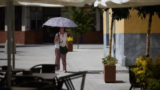 Una mujer se protege del sol con un paraguas cerca una terraza, en Talavera de la Reina.