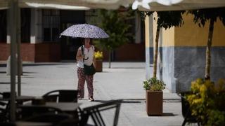 Una mujer se protege del sol con un paraguas frente a una terraza, en Talavera de la Reina.