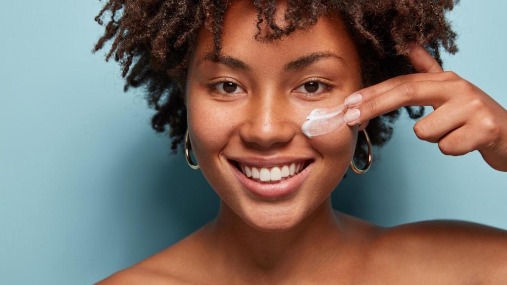 Mujer joven con corte de pelo afro aplicando crema en su rostro.