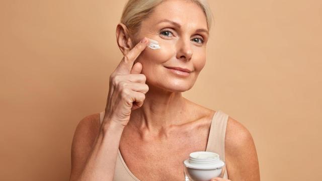 Mujer de mediana edad se aplica crema antienvejecimiento en la cara.