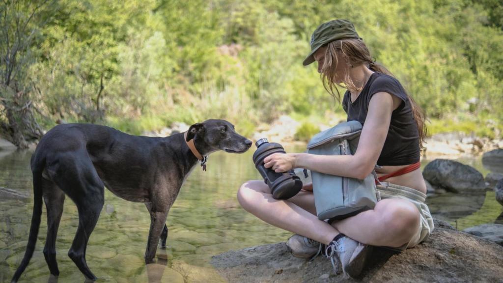 Una chica y un perro sentados cerca de un río.