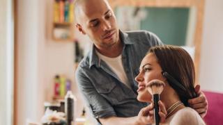 Maquillador aplicando colorete sobre una mujer.
