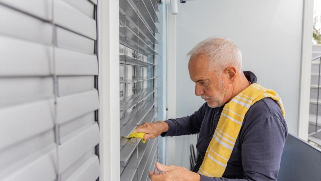 Un hombre limpiando las persianas.