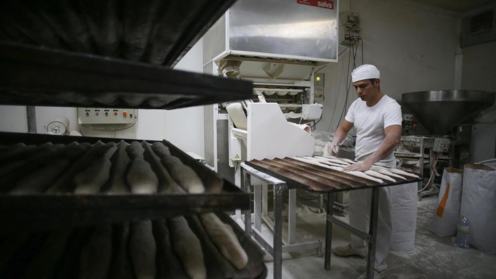 Un trabajador en un obrador preparando barras de pan.