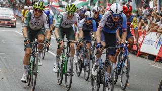 Un miembro del Israel Premier Tech en La Vuelta 2025 y, al fondo, una protesta propalestina