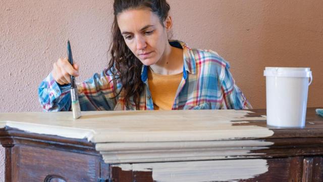 Mujer pintando un mueble de blanco.