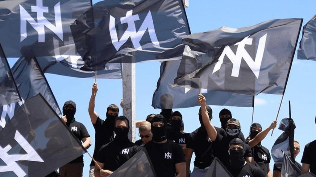 vestidos de negro, con estética paramilitar y la cara cubierta, portando banderas con su emblema.