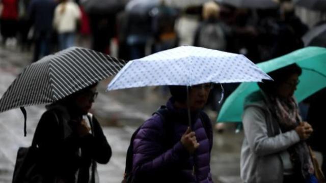 Varias personas se cubren de la lluvia con sus paraguas.