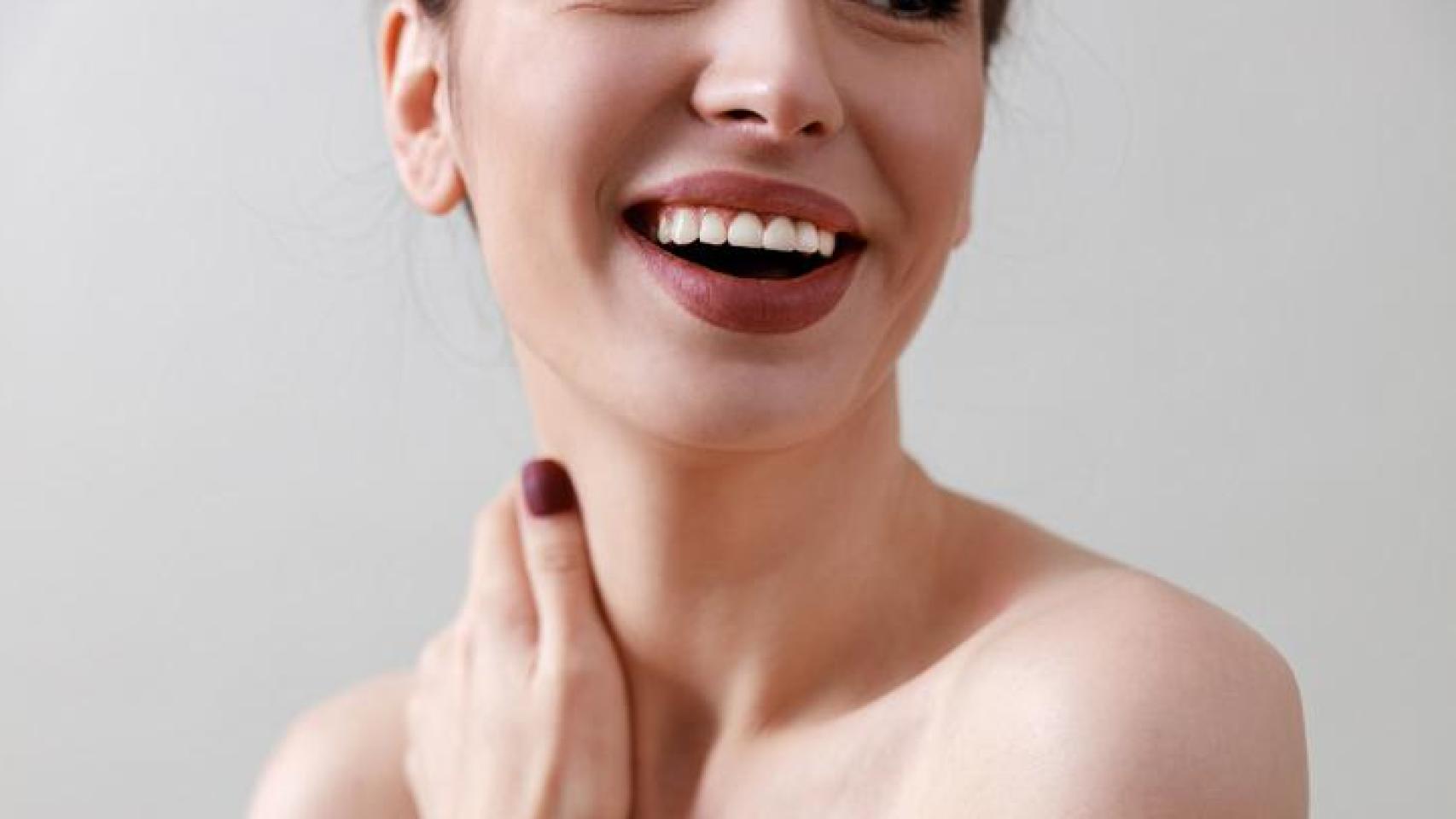 Mujer sonriente acariciándose el cuello.