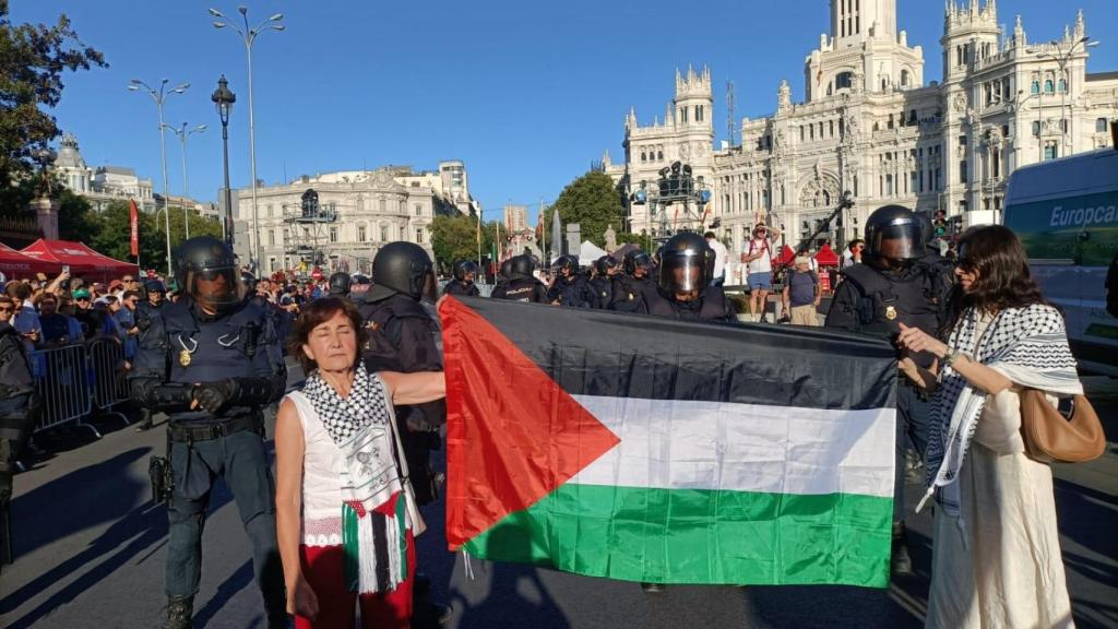 María de los Ángeles y Aznan sostienen una bandera frente al Ayuntamiento de Madrid y la Cibeles