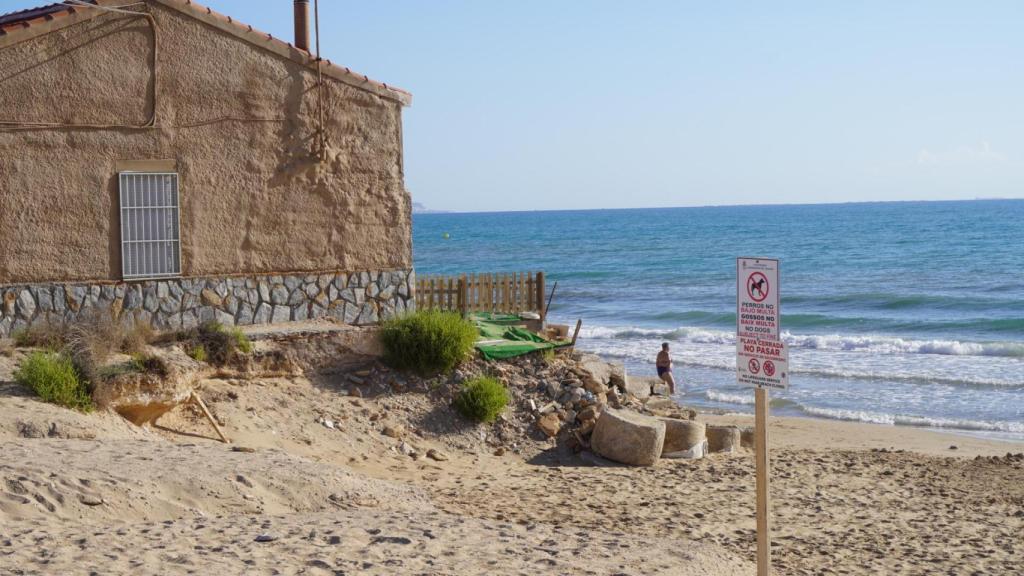 Un hombre en la playa junto a una de las viviendas afectadas.