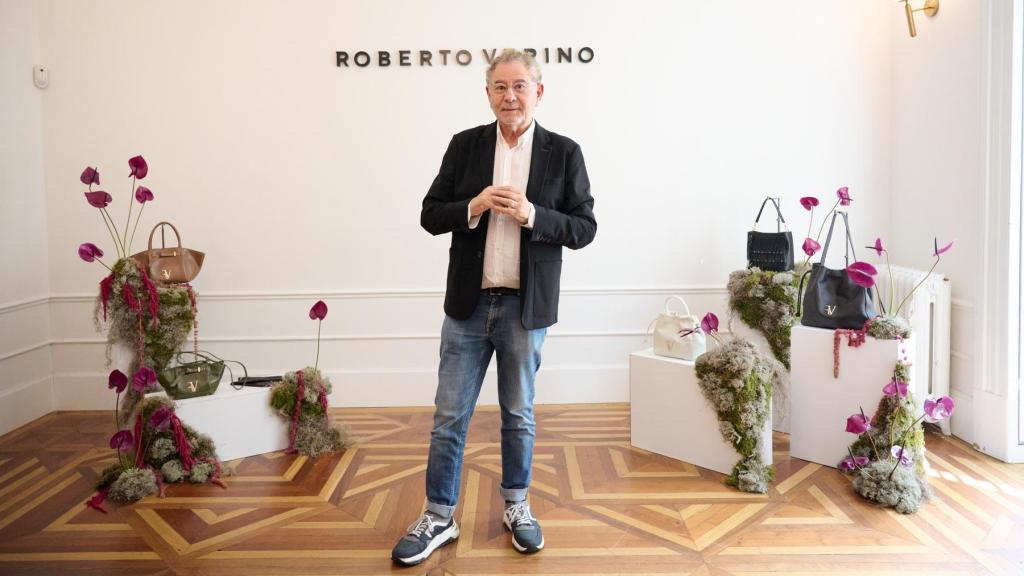 El creativo posando ante un bodegón compuesto por bolsos, flores y peanas.