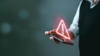 Imagen del símbolo de peligro sobre la pantalla de un teléfono móvil para ilustrar los riesgos en el mundo digital.