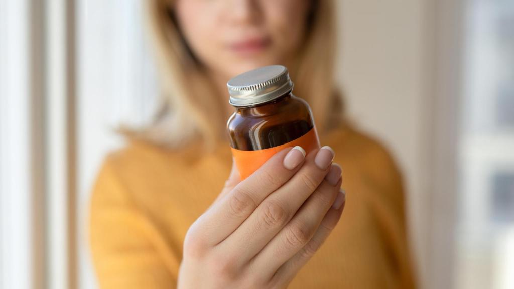 Mujer observando un frasco de vitaminas.