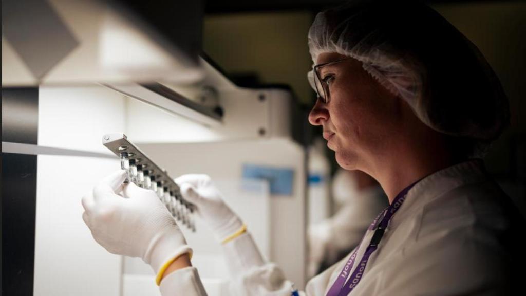 Una empleada de la farmacéutica sostiene un transportador de acero con viales de vacuna.