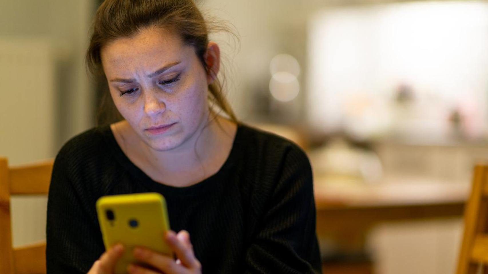 Una mujer estresada mirando las noticias y las redes sociales en el móvil.