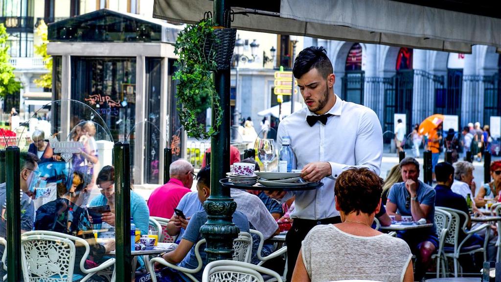 Camarero recogiendo los cubiertos y la cuenta de una mesa en una terraza de un café de Madrid.
