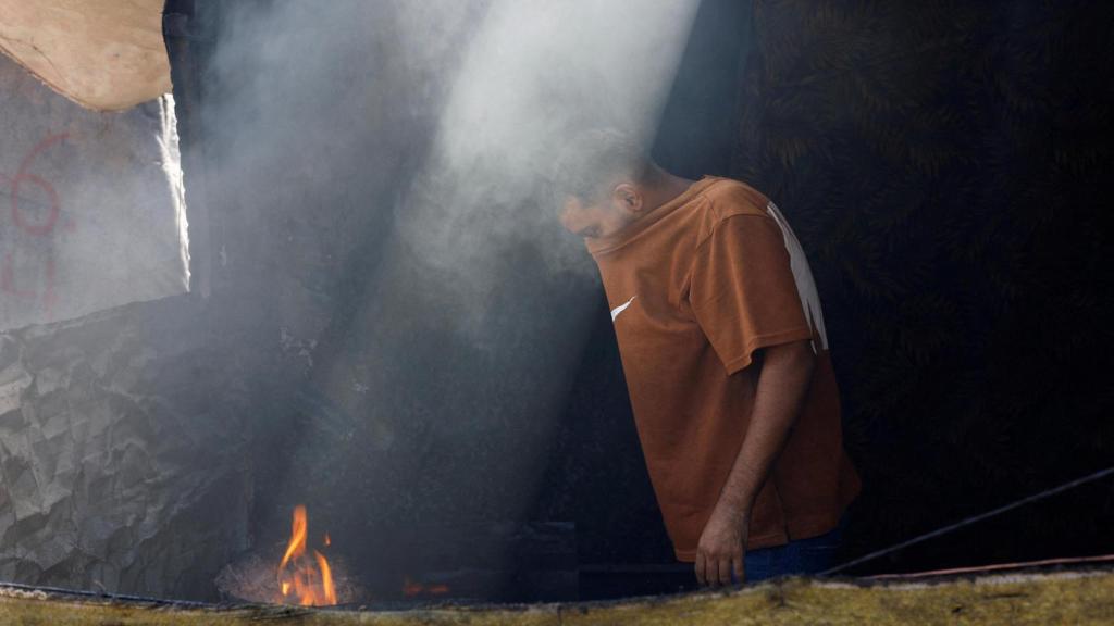 Un hombre palestino cocina comida sobre un fuego en su tienda de campaña, en Nuseirat.