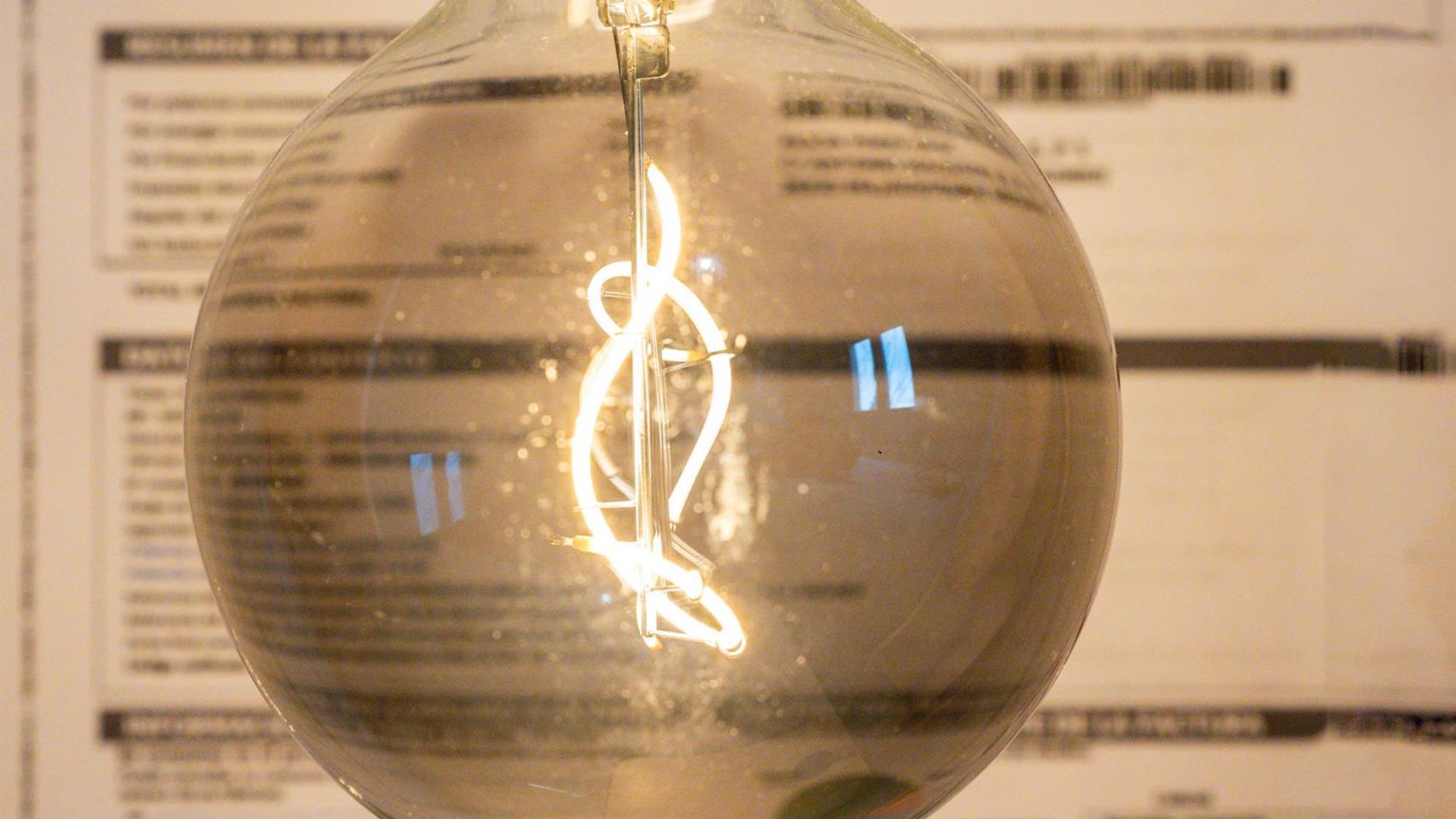 Una bombilla delante de una factura de la electricidad.