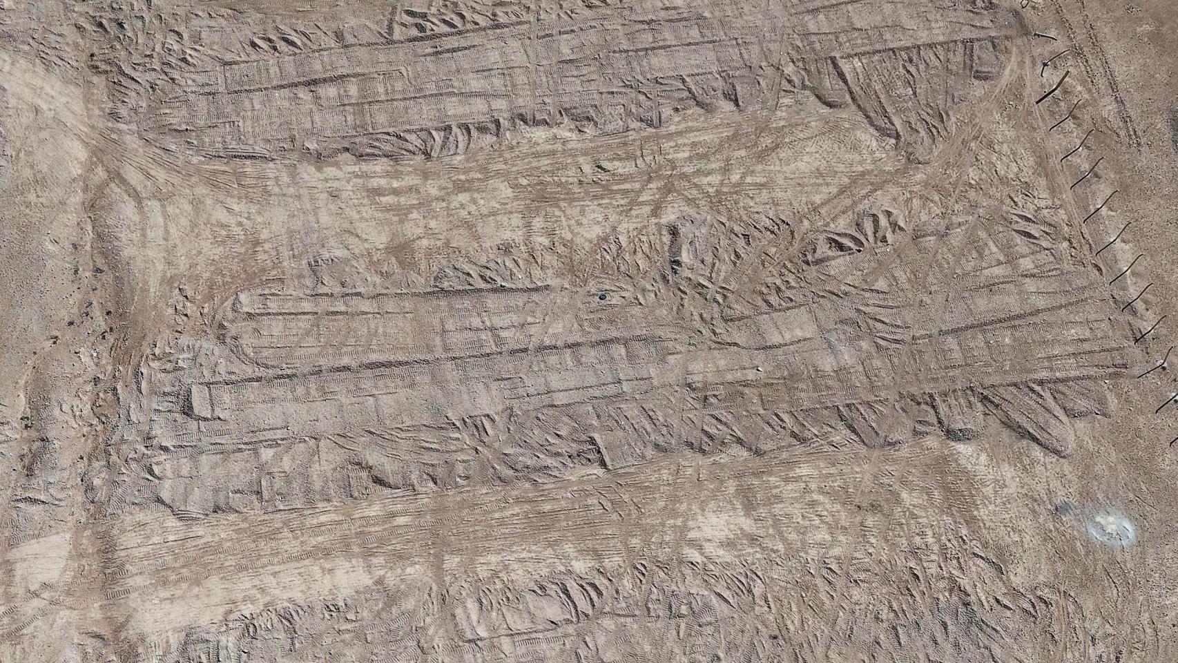 Vista aérea tomada con un dron las huellas dejadas por una excavadora en el suelo que cubre la fosa común en el desierto de Dhumair.