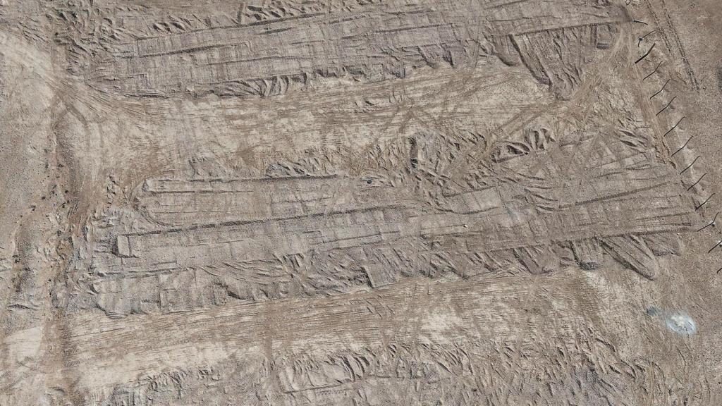 Vista aérea tomada con un dron las huellas dejadas por una excavadora en el suelo que cubre la fosa común en el desierto de Dhumair.