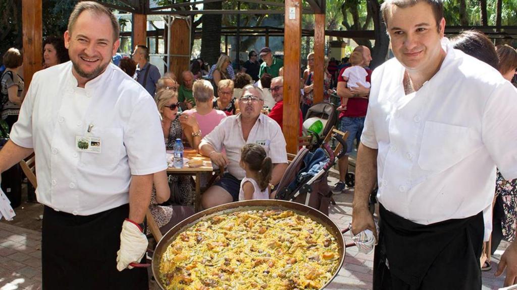 Dos trabajadores del restaurante La Garrofera sostienen una paella valenciana.