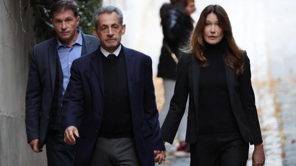 Nicolas y su mujer, de la mano, saliendo de su casa.