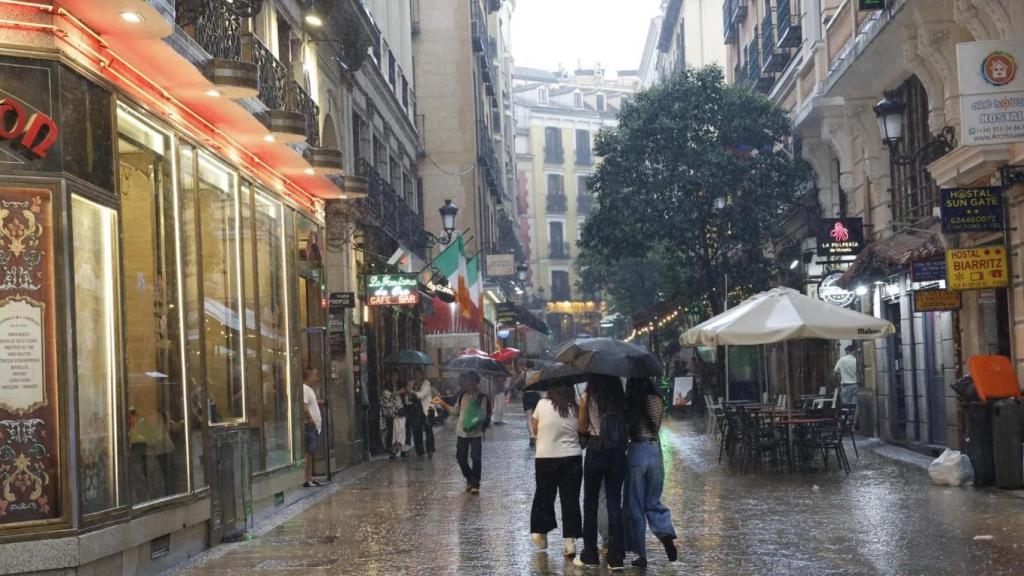 Varias personas se resguardan de la lluvia en una céntrica calle de Madrid.