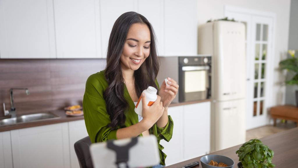 Imagen de archivo de una mujer tomando complementos alimenticios en la cocina.