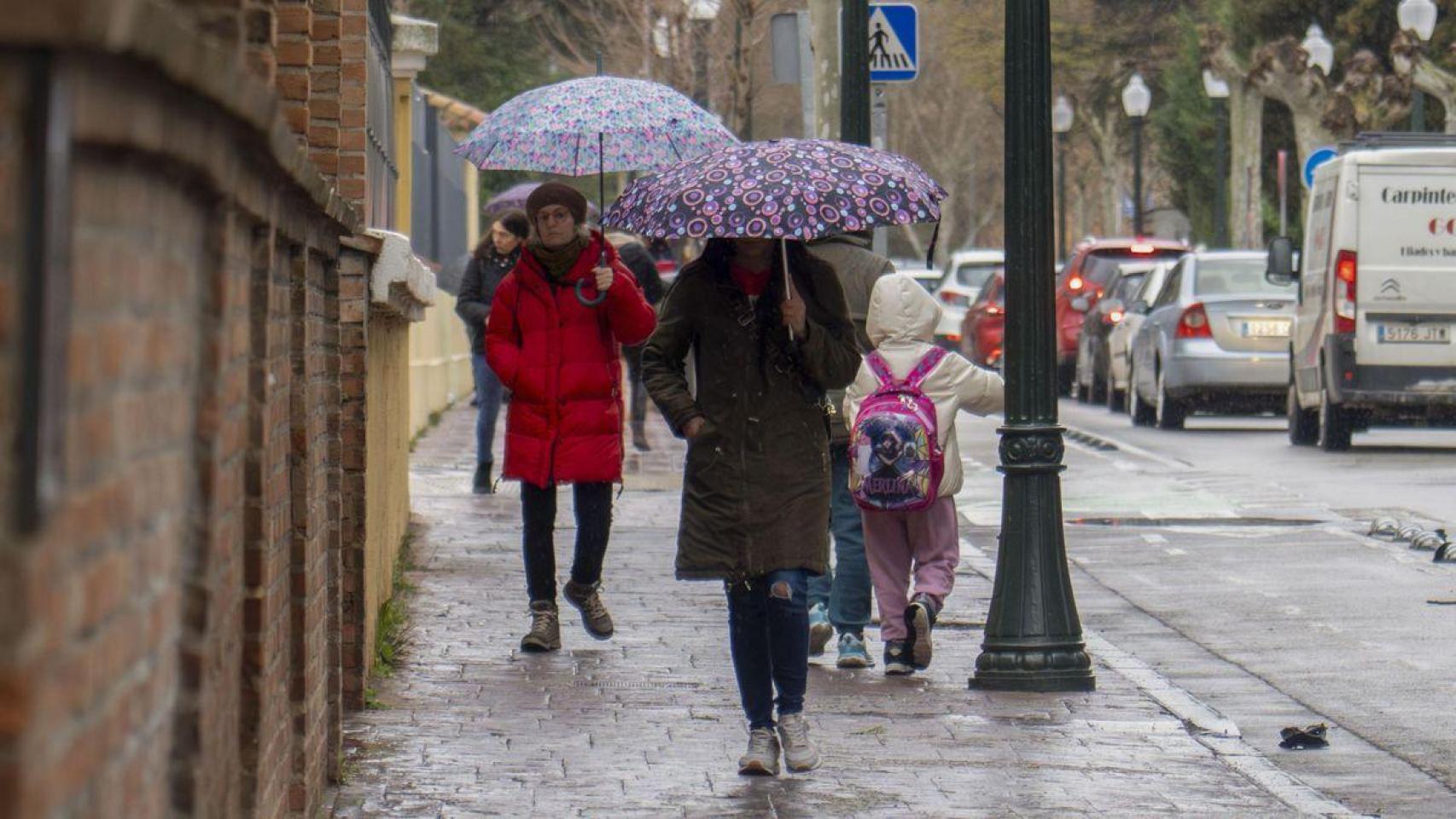 Varias personas con paraguas y abrigos caminando por Madrid.