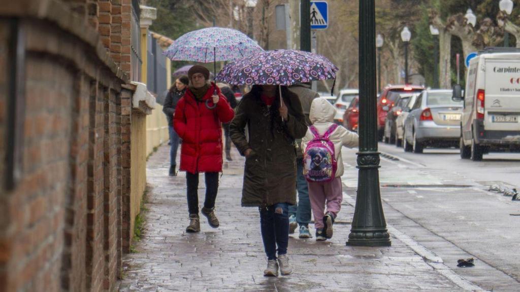 Varias personas con paraguas y abrigos caminando por Madrid.