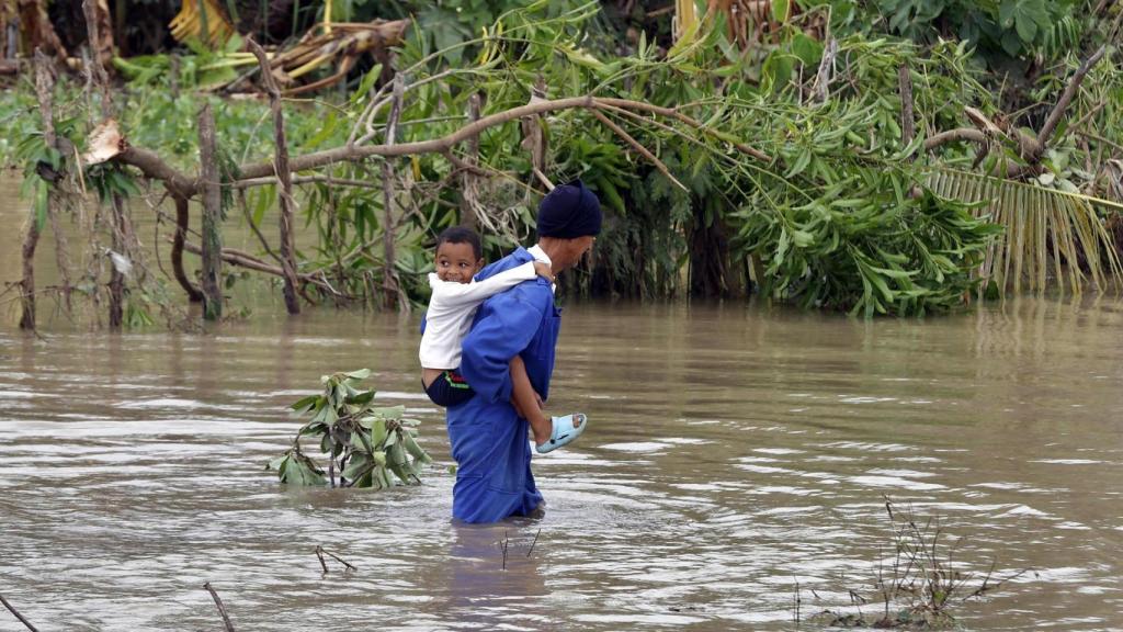 Un hombre cruza un río crecido mientras carga a un niño este miércoles, en el poblado de Guama en Santiago de Cuba (Cuba).