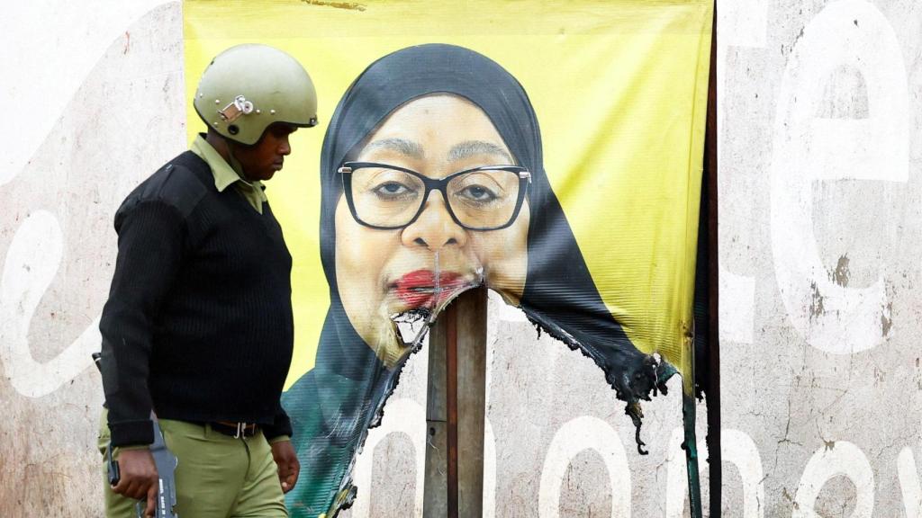 Un agente de la policía antidisturbios de Tanzania pasa junto a un cartel de campaña vandalizado de la presidenta Samia Suluhu.