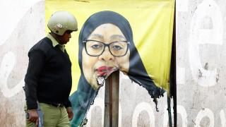 A Tanzanian riot police officer walks past a vandalized election banner for President Samia Suluhu.