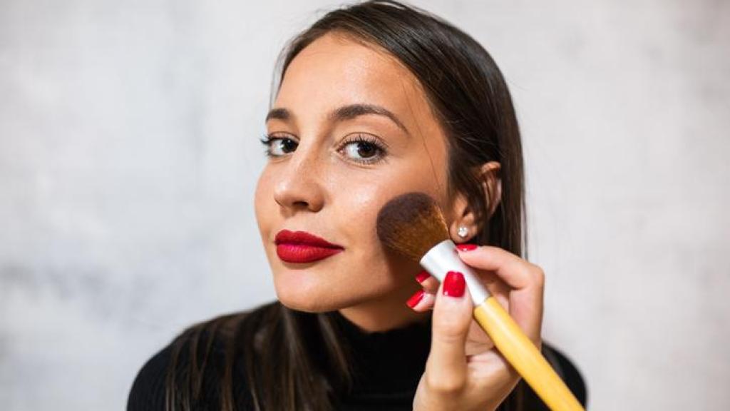Mujer aplicándose colorete con una brocha.