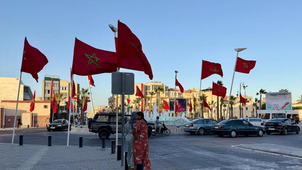 Dos mujeres esperan para cruzar la avenida Mohamed Hassan El Ouazzani, en el centro de Dajla, con una particular decoración llena de banderas del Reino de Marruecos.