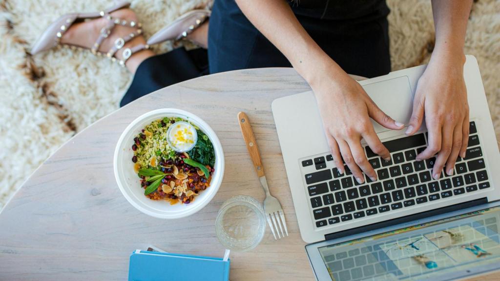 Imagen de archivo de una chica haciendo una comida rápida delante del ordenador.
