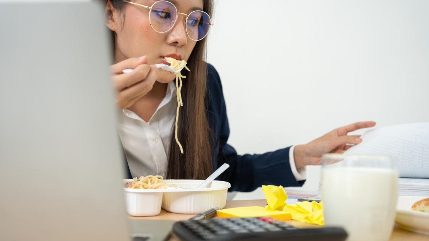 Imagen de archivo de una chica comiendo a la par que trabaja.