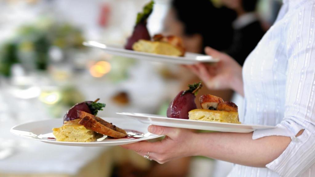 Una camarera lleva tres platos de comida a una mesa