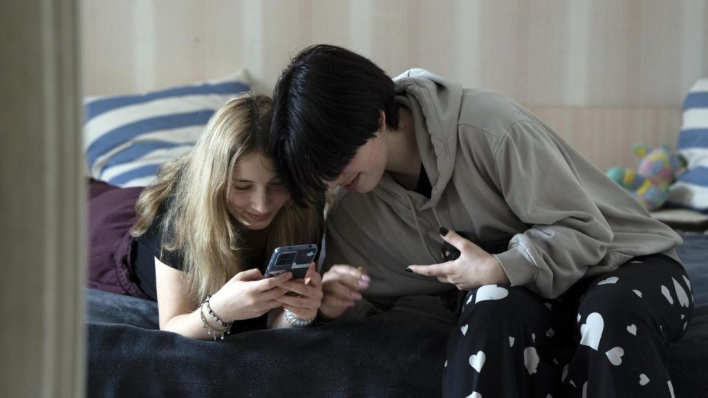 Dos adolescentes con los teléfonos en una cama.