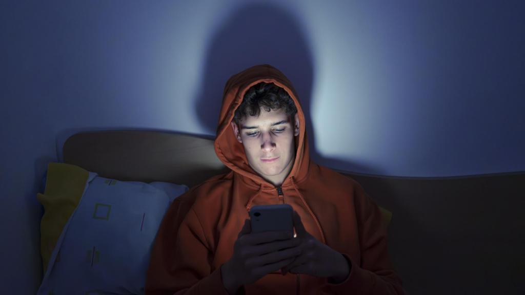 Un adolescente a oscuras usando el teléfono móvil.