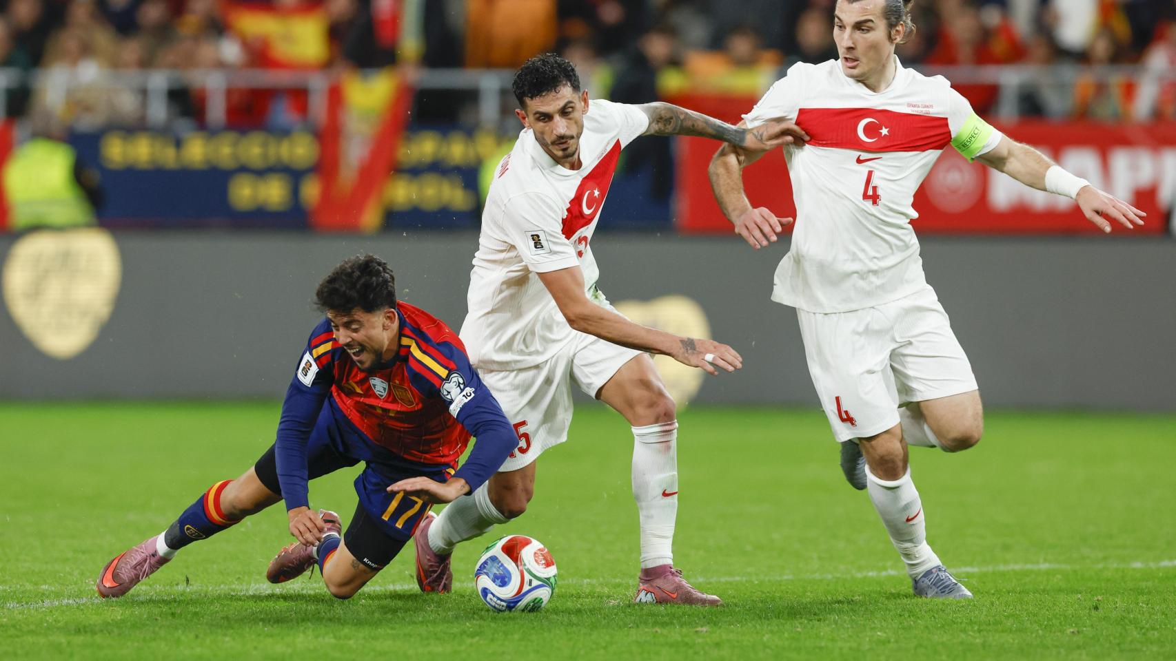 El centrocampista de la selección española de fútbol Pablo Fornals (i) cae tras chocar con Samet Akaydin (c), de la selección de Turquía, durante el encuentro correspondiente a la fase de clasificación para el Mundial 2026 que los combinados nacionales de España y Turquía disputan este martes en el estadio de La Cartuja, en Sevilla.