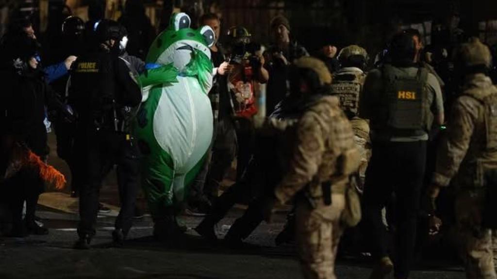 Una persona disfrazada de rana inflable observa cómo agentes del Departamento de Seguridad Nacional detienen a un manifestante en Portland.
