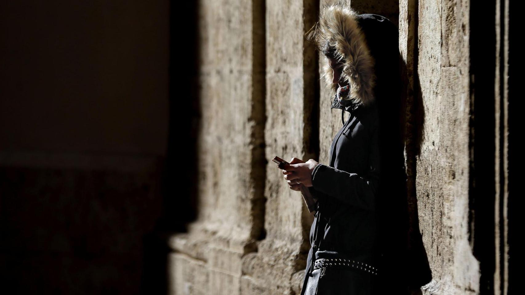 Imagen de archivo de una persona joven mirando su móvil en la calle.