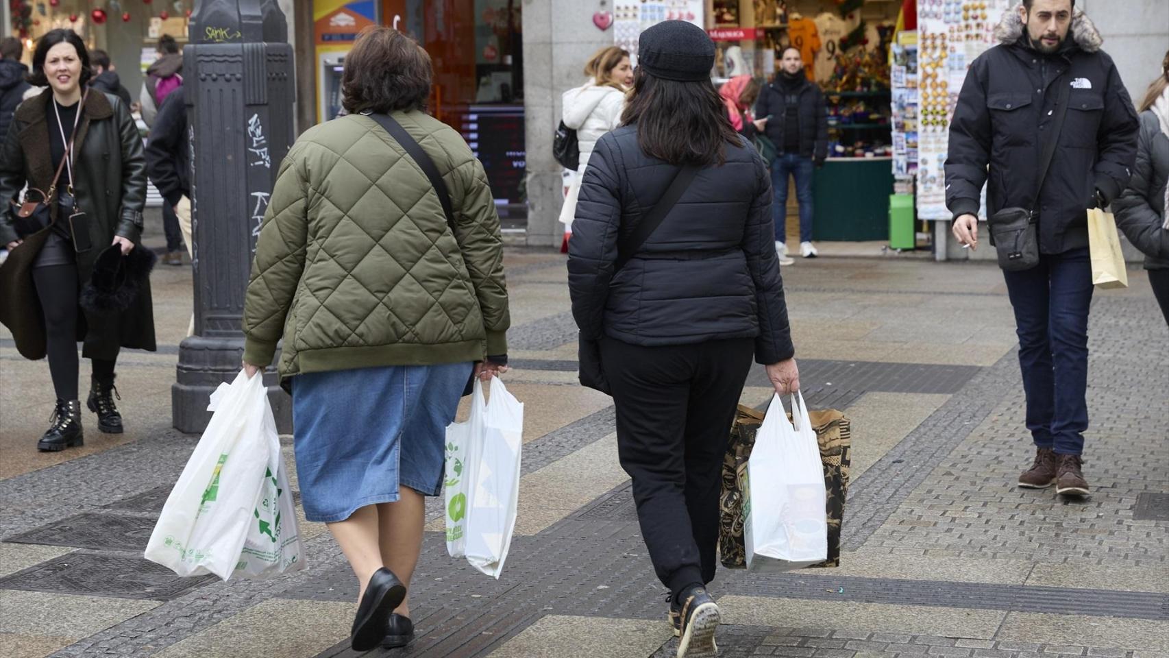 Dos mujeres pasean con bolsas de la compra.